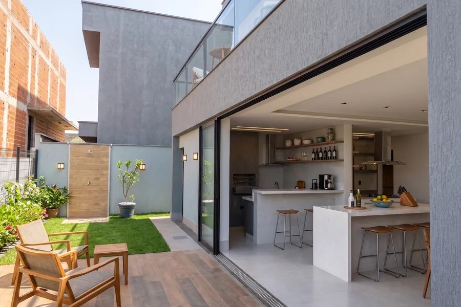 Área gourmet do Lar MH&D aberta para o jardim, com ilha e churrasqueira